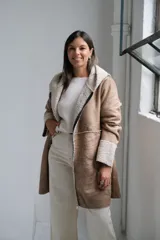 Tapado tipo gamuza con interior de corderito sintético, color beige con detalles en crudo. Presenta capucha, cierre frontal completo y puños con vuelta de corderito.