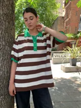Remera oversize a rayas horizontales marrones y blancas, con cuello polo y mangas cortas con ribete verde.