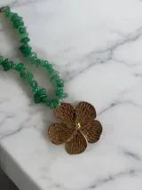 Collar con cadena de piedras irregulares en color verde y un dije central grande en forma de flor dorada con textura grabada.
