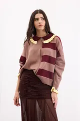 Cardigan de punto con cierre frontal de doble cursor, diseño a rayas horizontales en tonos bordó y beige. Presenta cuello estilo polo con volados en color amarillo y puños con el mismo detalle de volados.