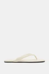 Sandalias planas tipo ojota de color beige, con tira delantera acolchada con separación para el dedo y suela fina.