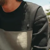 Buzo de cuello redondo Maui and Sons, con diseño de bloques de color en negro y gris. Presenta puños y ruedo acanalados, con un pequeño parche con el logo de la marca en el pecho.