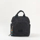 Mochila negra con diseño acolchado y pespuntes geométricos. Cuenta con un compartimento principal con cierre, un bolsillo frontal con cierre, asas superiores de mano y correas ajustables. Incluye un colgante decorativo con cuentas de colores en el lateral.