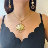 Collar con cadena dorada y dije colgante de sol con textura rugosa y una perla redonda engarzada en el centro.