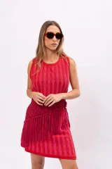 Vestido corto tejido a rayas verticales en tonos rosa y rojo, con cuello redondo y sin mangas. Incluye cinturón tejido con flecos.
