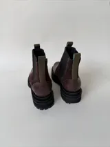 Botas tipo chelsea de cuero, combinando texturas en color bordó. Presentan paneles laterales elásticos en negro, suela track robusta y tiradores en la parte superior.