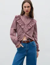 Camisa de manga larga con estampado de cuadros en tonos rojizos, cuello mao y detalle de volados en el frente. Cuenta con cierre frontal de botones y puños con volados.