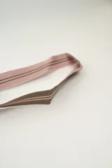 Cartera tipo saco con estampado geométrico en tonos rosados y marrones, con cierre de cordón fruncido y asa de hombro.