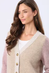 Saco tipo cárdigan de tejido grueso con diseño en bloques de color, combinando tonos beige y rosado. Presenta cuello en V, cierre frontal con botones y dos bolsillos delanteros.