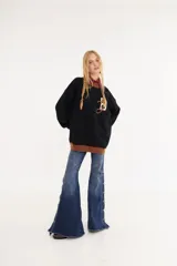 Sweater de punto color amarillo con silueta oversize y estilo universitario vintage. Presenta cuello redondo, puños y ruedo en tejido acanalado de color gris azulado, y un diseño gráfico bordado en el frente.