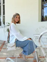 Cartera tipo sobre color crudo, confeccionada en cuero, con correa larga de cuero marrón y costuras decorativas en contraste.