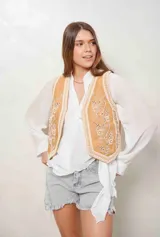 Chaleco de denim color camel con bordados florales en blanco y aplicaciones de perlas en el frente.
