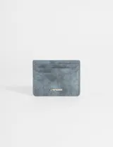 Tarjetero de cuero vegano con textura gamuzada en color gris azulado, con múltiples ranuras para tarjetas y logo metálico de la marca en el frente.