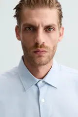 Camisa blanca de manga larga con cuello italiano y cierre frontal de botonadura. Corte regular fit.