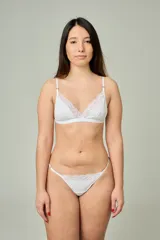 Conjunto de lencería blanco de algodón y encaje, compuesto por un bralette triangular con detalles de encaje en los bordes y breteles regulables, y una tanga colaless a juego con apliques de encaje en la parte frontal y tiras laterales regulables con argollas metálicas.