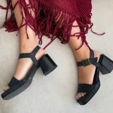Sandalia de cuero vacuno color negro, con taco ancho de 7 cm y plataforma de 2 cm. Diseño de punta cuadrada, con tira ancha en el empeine y tira ajustable con hebilla en el tobillo.