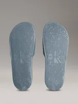 Ojotas tipo slide de Calvin Klein Jeans en color azul, con logo de la marca en relieve en color verde neón sobre la banda superior y logo grabado en el lateral de la suela.