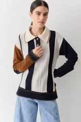 Buzo de punto estilo polo con diseño de rayas verticales en tonos azul marino, crema y marrón. Presenta cuello camisero, cartera frontal con botones, mangas largas con coderas en contraste y tajos laterales en el ruedo.