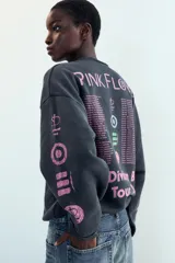 Sudadera de cuello redondo y manga larga con efecto lavado, color gris oscuro. Presenta un estampado frontal con el diseño de "The Division Bell Tour '94" de Pink Floyd y detalles estampados en las mangas. Cuenta con acabados en rib y bordes con efecto desgastado.