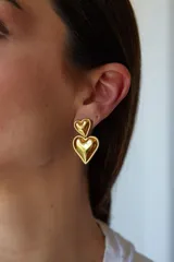 Aros de metal dorado con diseño colgante de doble corazón abombado y acabado brillante.