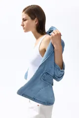Blazer de denim de algodón celeste, con solapas de muesca, hombreras y mangas tres cuartos fruncidas. Cuenta con bolsillos delanteros con solapa y diseño abierto sin cierre.