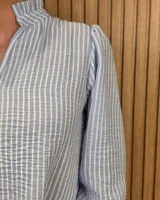 Blusa blanca de algodón con escote en V y cuello mao. Presenta mangas largas abullonadas con puños acampanados y fruncidos.