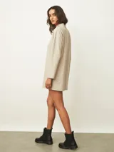 Vestido corto de color beige con cuello alto y mangas largas, de corte recto y holgado.