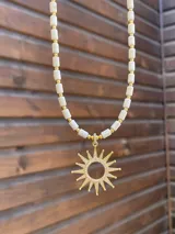 Collar dorado con baño de oro y piedras reconstituidas blancas en forma de cuentas cilíndricas, con un dije colgante en forma de sol con incrustaciones de circones.