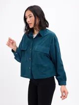 Campera de pana color verde petróleo, con cuello camisero, cierre frontal de botones, bolsillos frontales con solapa y mangas largas con puños abotonados.