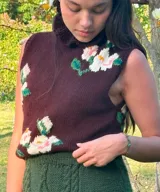 Chaleco de lana merino color marrón bordó, de tejido artesanal con cuello alto tipo gorguera y estampado floral.