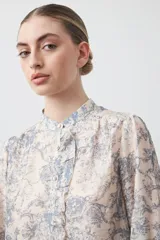Camisa de manga larga con cuello con volados y botones nacarados. Presenta un estampado romántico de inspiración barroca en tonos azul y beige.