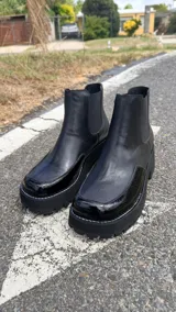 Botas chelsea de cuero color negro, con puntera de charol, elásticos laterales y suela flatform track con pespunte blanco.
