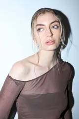 Remera de manga larga y escote asimétrico, confeccionada en tul negro transparente. Lleva un top negro opaco debajo y un cinturón de cadena plateada a la altura de la cadera.