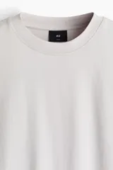 Remera boxy de punto de algodón pesado, color gris claro, con cuello redondo ribeteado acanalado, hombros caídos y mangas cortas de corte holgado.