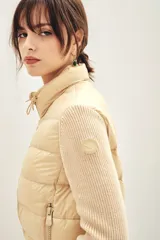 Campera puffer color beige con cuerpo acolchado y mangas tejidas de punto. Presenta cuello alto, cierre frontal y bolsillos laterales.