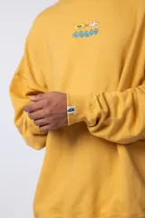Buzo de cuello redondo y corte oversize, confeccionado en tela rústica color amarillo. Presenta un pequeño estampado central en el pecho con un avión y olas.