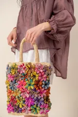 Bolso tipo tote color beige con flores tejidas multicolor en relieve, doble asa corta de mano y diseño rectangular.