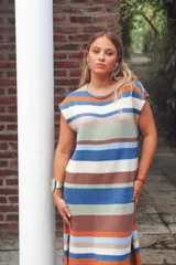 Vestido largo de tejido de punto, con rayas horizontales en tonos tierra, azul y blanco. Presenta cuello redondo, mangas cortas caídas y aberturas laterales en el ruedo.