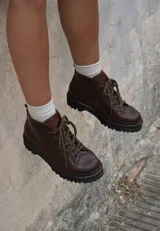 Borcegos de cuero charolado negro con cordones jaspeados en tonos marrones y suela track dentada con costura blanca visible.