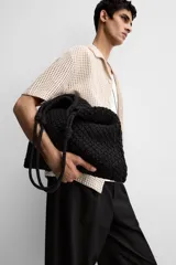 Bolso tipo shopper color crudo, confeccionado en tejido trenzado de algodón con diseño de macramé. Cuenta con dos asas de hombro ajustables que funcionan como cierre del compartimento principal.