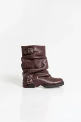 Botas de caña media confeccionadas en cuero color marrón oscuro, con diseño arrugado y dos correas con hebillas metálicas ajustables. Presentan suela plana de goma negra con un pequeño taco cuadrado.