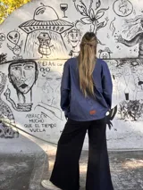 Sobre camisa de gabardina símil denim, color azul, con costuras visibles en color rojo y etiqueta de cuero en la espalda. Presenta un corte holgado y mangas largas.