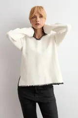 Sweater de punto color crudo con escote en V, manga larga y detalles de bordado en color negro en el escote y los puños.