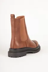 Bota Chelsea de cuero sintético color negro, con elástico lateral, puntera redondeada con detalle de perforaciones y suela track.