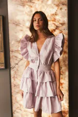 Vestido corto de lino color lila, con escote en V, mangas cortas con volados y falda escalonada con volados.
