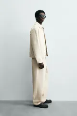 Pantalón chino de algodón color beige, de corte relajado (relaxed fit) y tiro medio. Presenta bolsillos delanteros y bolsillos traseros de vivo con cierre de cremallera y botón.