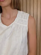 Musculosa de lino color blanco, de corte holgado, con cuello en V, detalles de tablas y frunces en los hombros, y dobladillo desflecado.