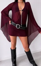 Vestido corto de tul color bordó con escote profundo en V y mangas largas acampanadas con puños ajustados. Presenta un diseño traslúcido y fluido.