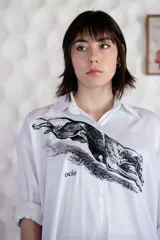 Camisa blanca de algodón con estampado de un galgo y la palabra "ocio" en el frente. Manga larga con puños y botones.