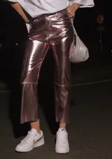 Pantalón de ecocuero con acabado metalizado en color rosado, de corte capri semi oxford y tiro medio-alto. Presenta cierre frontal con botón metálico y bolsillos traseros.